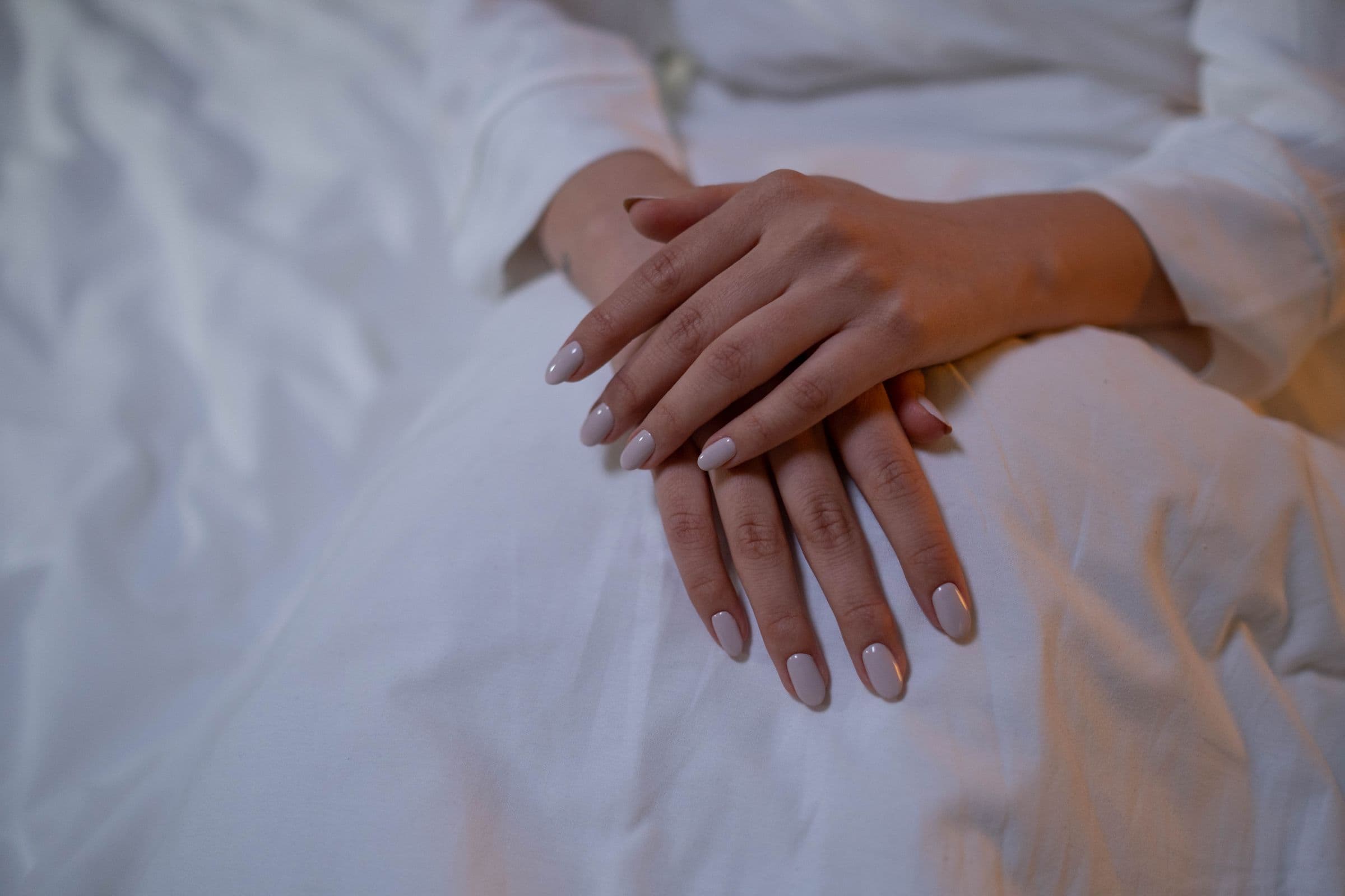 Mains croisées aux ongles nude sur lin blanc